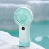 Smart Digital Display Portable Rechargeable Handheld Desktop Fan, showing its white body, warm beige front grille, LED digital display screen, side charging port, and wavy base stand.