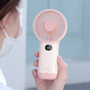 Smart Digital Display Portable Rechargeable Handheld Desktop Fan, showing its white body, warm beige front grille, LED digital display screen, side charging port, and wavy base stand.